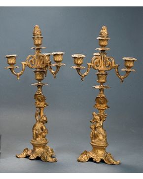 22-Pareja de candelabros de bronce dorado. de tres luces y apagavelas. con fuste adornado por represenatción de niño y niña en bulto redondo.