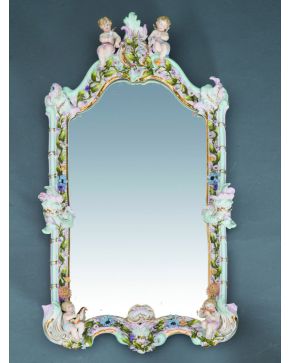 70-Espejo con marco en porcelana de Sajonia. C. 1900. Decoración vegetal y floral con copete flanqueado por amorcillos que sostienen flores y otros dos e