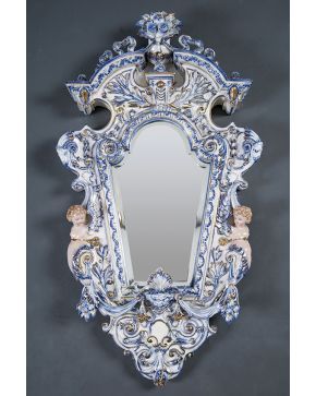 1528-Espejo de pared italiano en porcelana esmaltada azul y blanca con detalles en dorado. Decoración en relieve de niños en los laterales. cabezas de carn