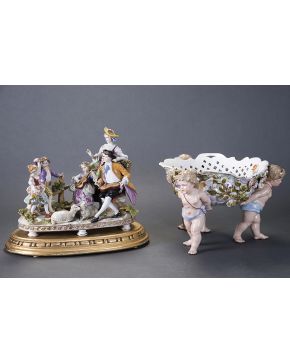 975-Centro de mesa en porcelana siguiendo modelos de Meissen. con tres angelotes a modo de patas sosteniendo una cesta. Decoración de rosas modeladas en e