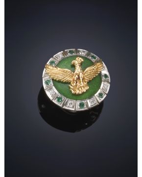 136-INSIGNIA DE ÁGUILA EN ORO AMARILLO DE 18K SOBRE FONDO DE ESMALTE VERDE Y ORLA DE BRILLANTES Y ESMERALDAS. Montura en oro blanco de 18k.