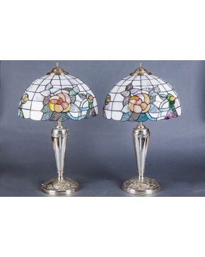 932-Elegante pareja de lámparas de sobremesa con fuste en plata de ley 925 con decoración en relieve de flores y lazos. Pantallas de cristal emplomado tip