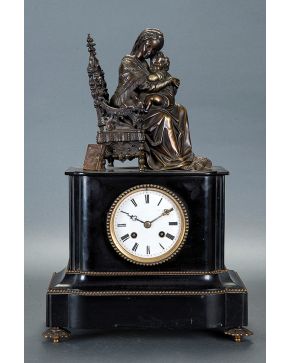 2119-Reloj de sobremesa Napoleón III en mármol negro con figura en bulto redondo de maternidad en bronce pavonado de remate, siglo XIX. Esfera en porcelana blanca con numeración romana en negro. Maquinaria de cuerda a llave. 