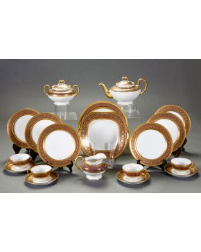 527-Vajilla de merienda en porcelana francesa de Limoges, con marcas W.C. & Co. Friso decorado en tonos granate y filos en dorado. Compuesta por: 10 tazas con 12 platillos, 11 platitos llanos, bandeja cuadrada con asas, fuente circular, cafetera, lec