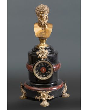 861-Reloj francés, c. 1850. En mármol negro belga y jaspe rojo con patas y aplicaciones en bronce, al igual que el busto clásico que corona la pieza (¿Hércules?).