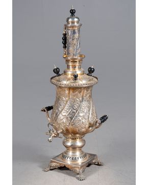 359-Samovar en metal plateado. Marcas árabes. Cuerpo gallonado con flores repujadas, asas torneadas en madera, remate en cuero cilíndrico y base cuadrada sobre patas de garra.  Altura: 89 cm.