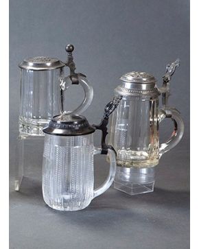 2174-Lote de tres jarras de cerveza o Tankard, en cristal centroeuropeo y metal con tapas bellamente adornadas con inscripciones, escudos y paisajes. Altura mayor: 20 cm.