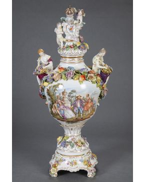 771-Gran jarrón con tapa en porcelana de Viena, c. 1900. Con marcas. Con escenas galantes en el cuerpo, personajes femeninos en bulto redondo con cestos de flores a modo de asas y putti  con escudo