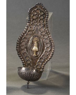 474-Antigua benditera en plata, fines s. XIX. Decoración cincelada de flores y elmentos vegetales, con la representación de la Virgen del Pilar. Alguna consolidación.  Peso: 124 gr.  Altura: 26 cm.