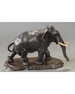 1157-Elefante en bronce pavonado. Sobre peana en madera tallada. Medidas: 23x40x12 cm.