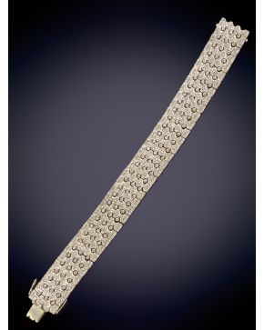 666-EXQUISITO BRAZALETE ARTICULADO CON PLACAS CUAJADAS DE BRILLANTES UNIDAS ENTRE SÍ POR TRES CHATONES sobre una montura en oro blanco de 18