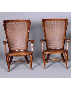 2210-Pareja de butacas orejeras en madera con respaldo y asiento de rejilla, una de ellas con desperfectos en la rejilla del asiento. Altura: 97 cm.