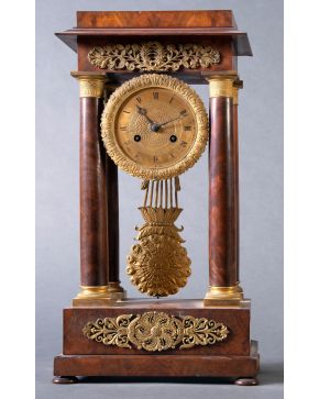 1138-Reloj de sobremesa, Francia s. XIX, estilo Napoleón III en madera de raiz y bronce dorado. Esfera enmarcada en columnas con cumeración 