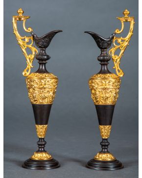 688-Pareja de jarras historicistas, s. XX, en metal dorado y pavonado con decoración de hojas de acanto, mascarones, camafeos y lazos.  Altura: 36 cm.