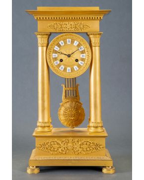 701-Reloj de pórtico en bronce dorado, Carlos X, Francia, C. 1830. Esfera entre columnas  y frisos con motivos vegetales en relieve. Con péndulo y lla