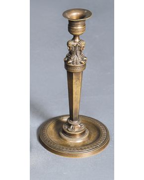 2481-Candelero Imperio en bronce pavonado con fuste a modo de columna coronada por efigies y pies en