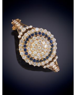 429-BELLA PULSERA CON GRAN ROSETÓN DE BRILLANTES CON ORLA DE ZAFIROS SOBRE UNA MONTURA RÍGIDA EN ORO AMARILLO DE 18K. 