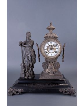 2380-Antigua guarnición decorativa compuesta por reloj de sobremesa inglés y escultura de dama con arpa en metal sobre base pintada en negro