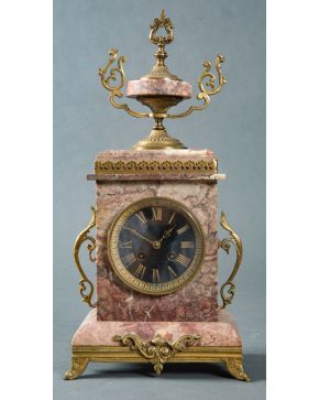 2247-Reloj de sobremesa francés, estilo Luis XVI, en mármol rosa con remate de copa en bronce dorado.  Altura: 46 cm. 